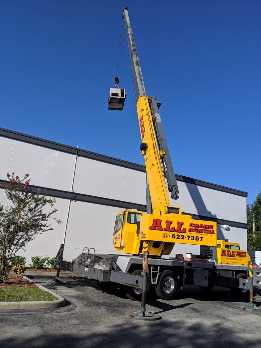 Yellow crane lifting a suspended cage beside a building under a clear blue sky