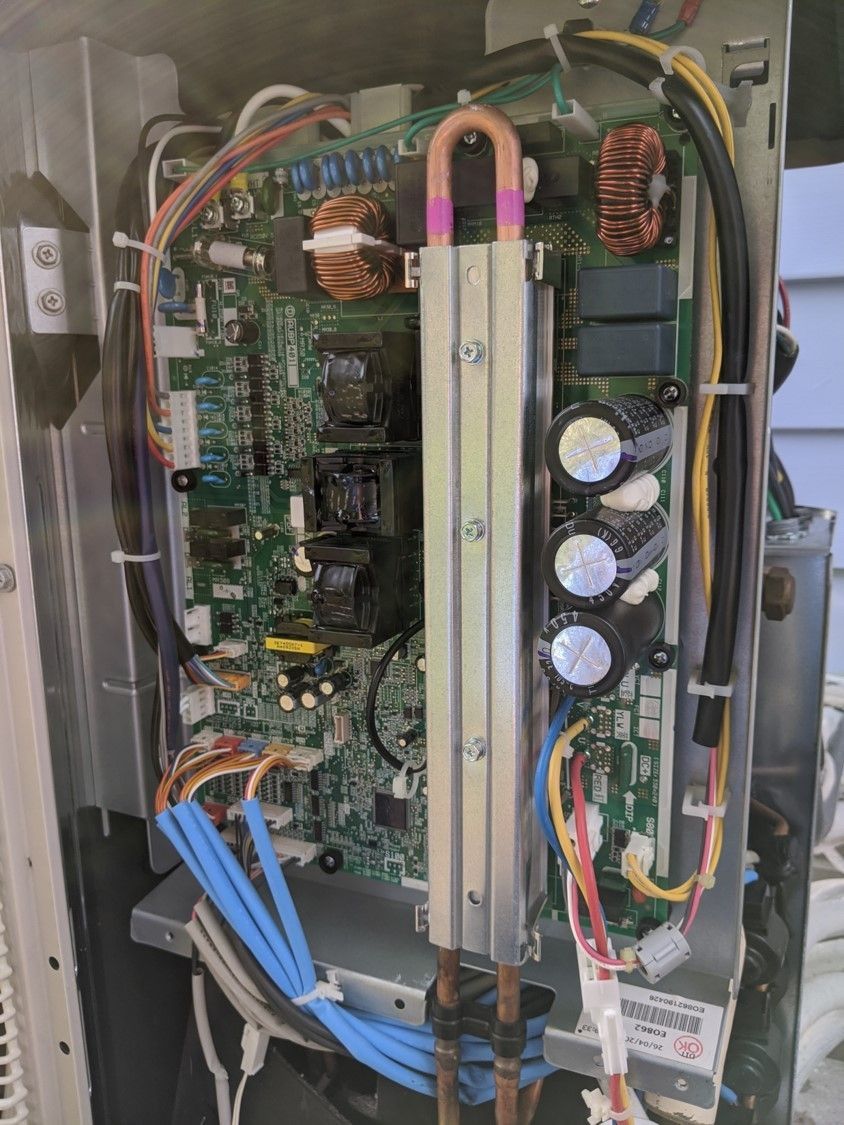 Open electrical panel with circuit boards, wiring, and capacitors mounted inside a metal enclosure