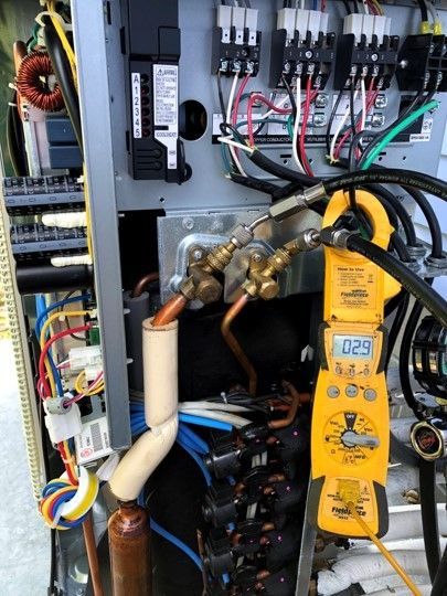Electrical panel interior with yellow multimeter and copper refrigerant lines during service work
