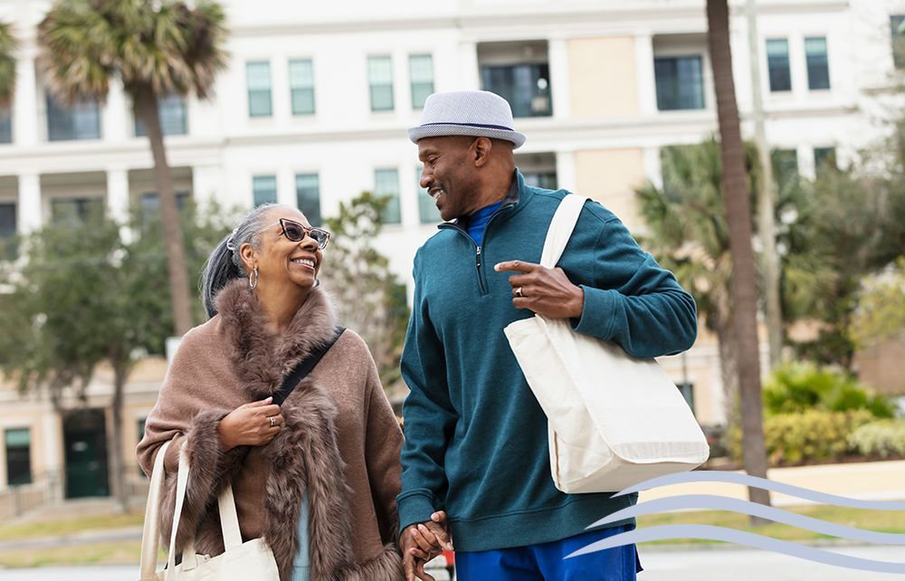 Two people walking and smiling outdoors, carrying tote bags in front of a white building