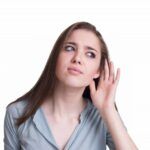 Woman in a blue shirt cupping her ear, looking confused or listening intently on a white background