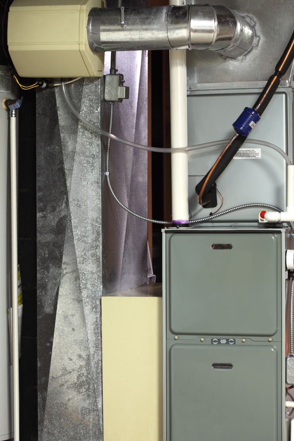Basement utility area with a gray furnace, metal ductwork, and exposed pipes against a concrete wall