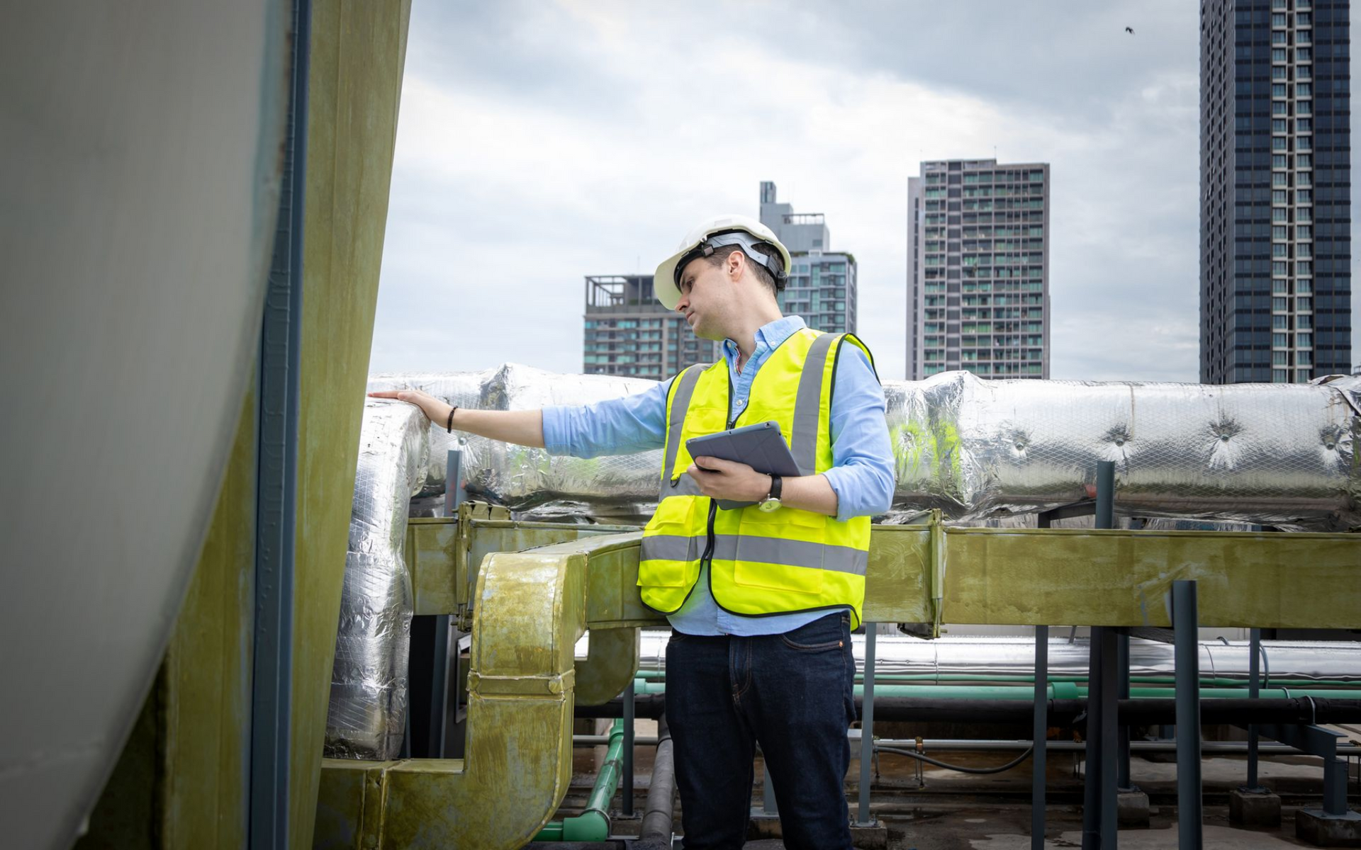 Worker in yellow safety vest inspecting industrial piping on a rooftop.