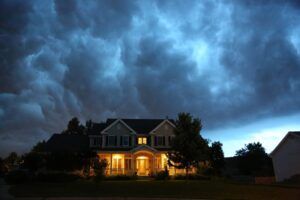 House glowing at night under dramatic storm clouds, with lit porch and dark trees silhouetted around it