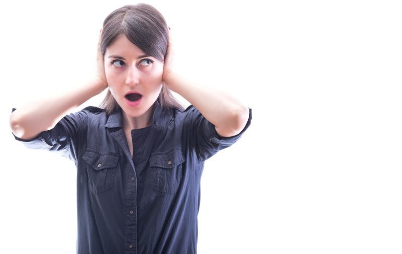 Woman in a dark shirt covering her ears, looking upset against a white background
