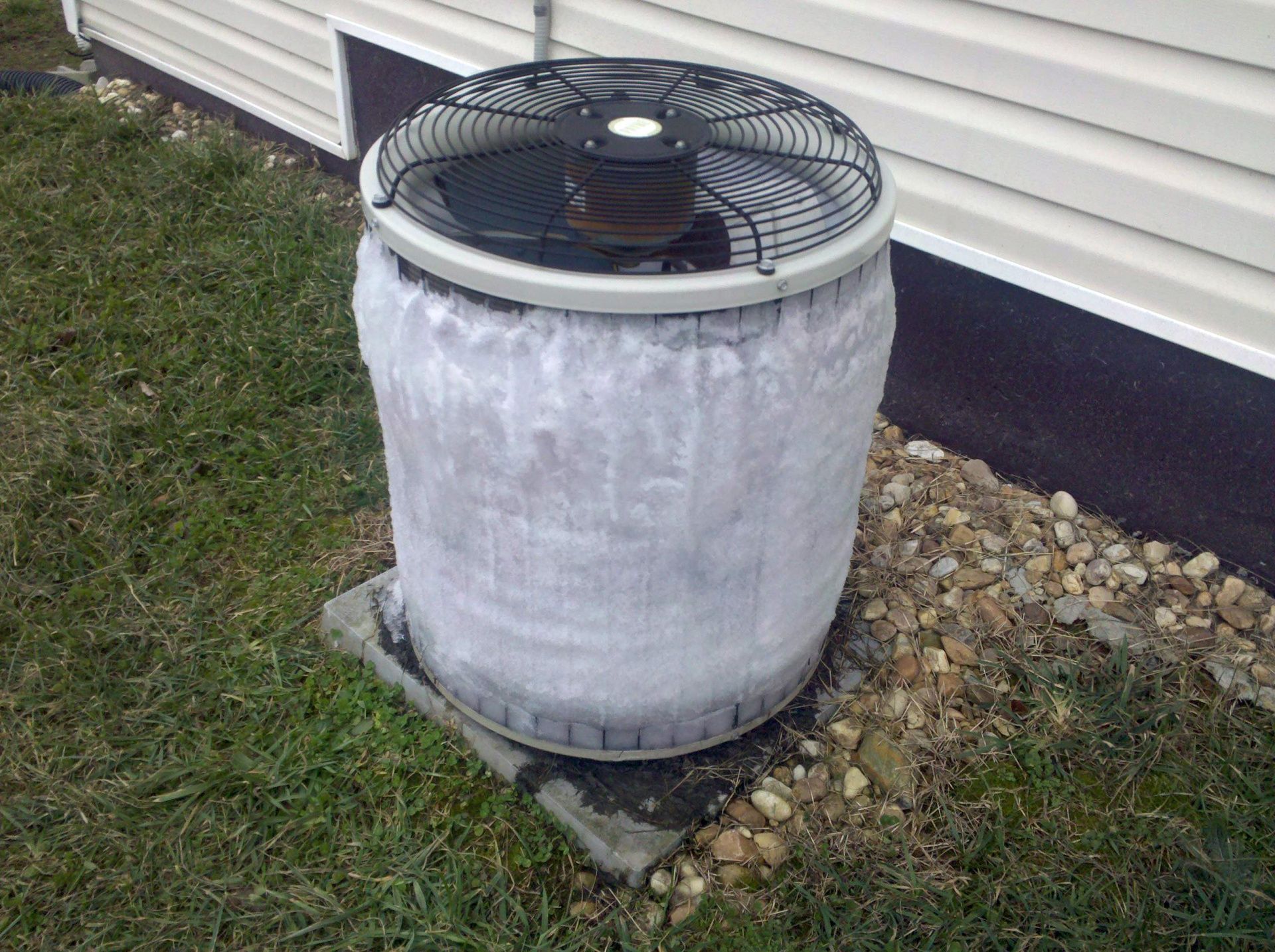 Outdoor air conditioner unit with heavy frost buildup on top and sides beside a house wall.
