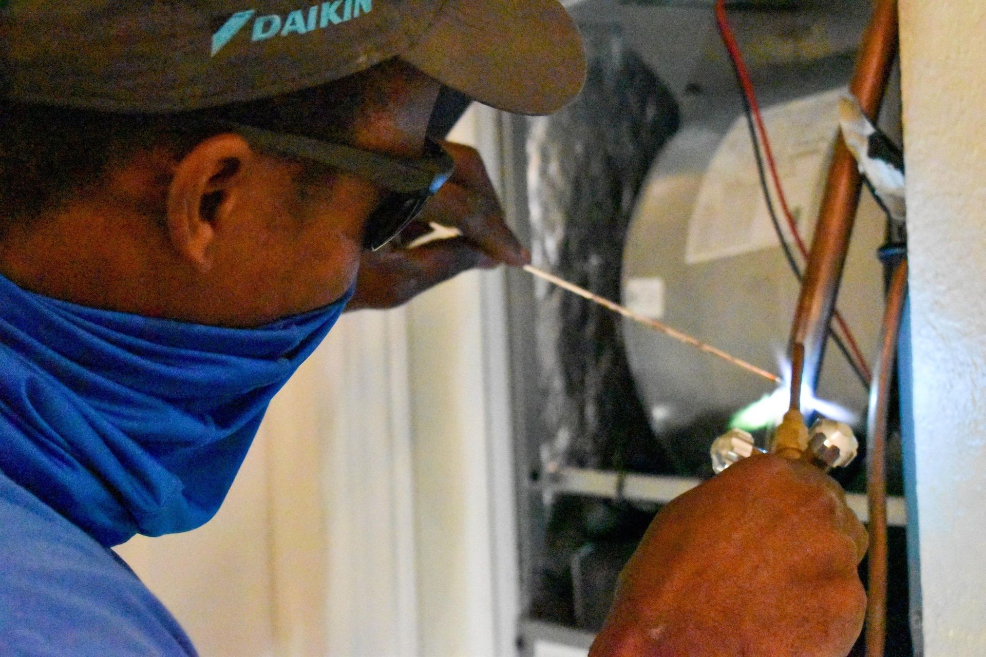 Worker in a hard hat and blue face covering using pliers on copper pipes indoors