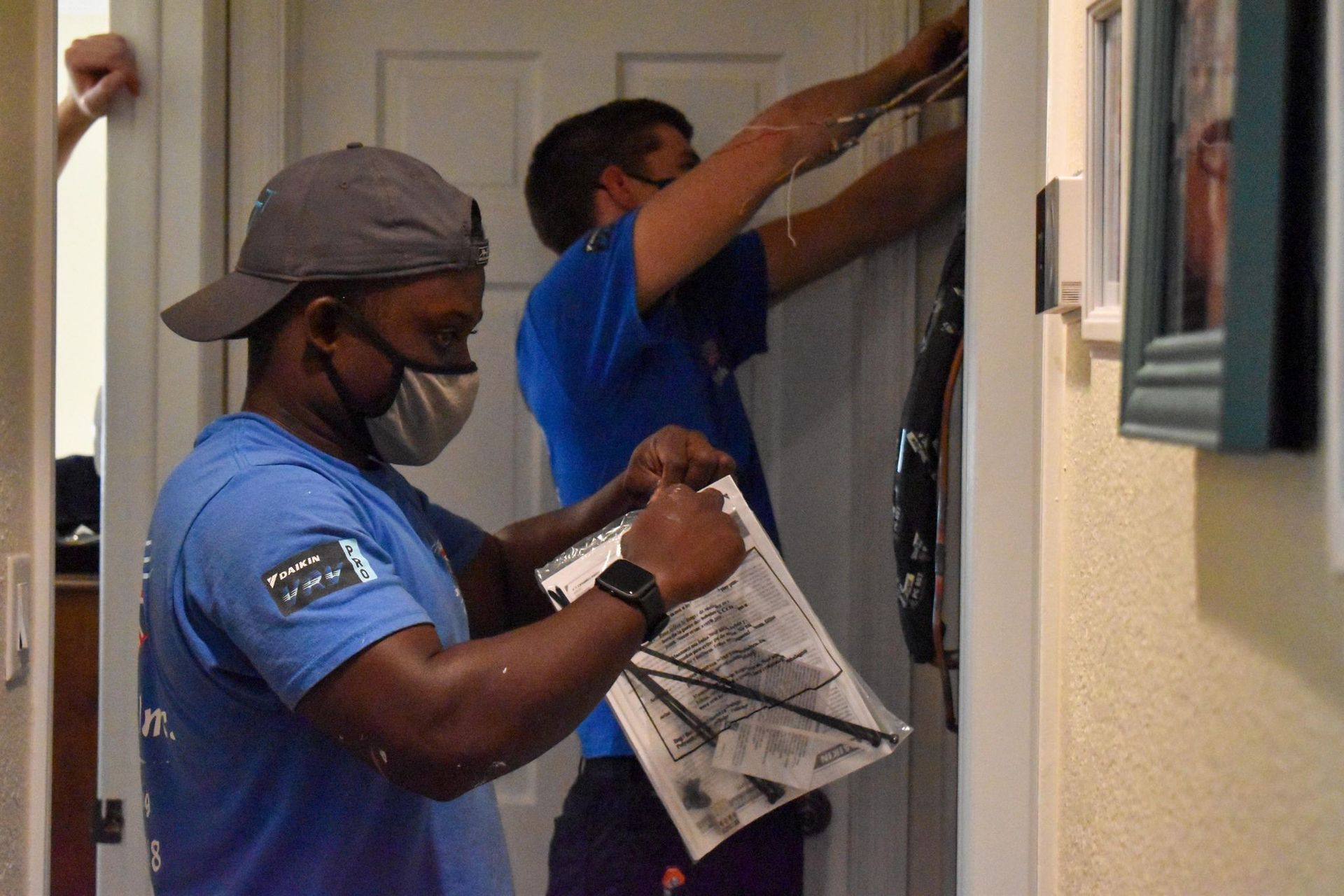 Two workers in blue shirts fixing a closet door, one holding instructions and the other reaching up.