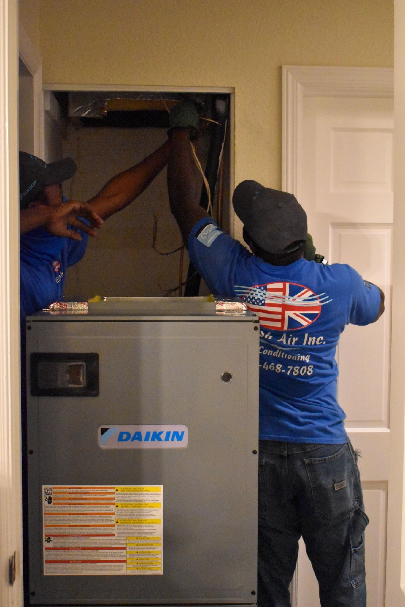 Two workers installing a Daikin HVAC unit in a closet opening with exposed ductwork.