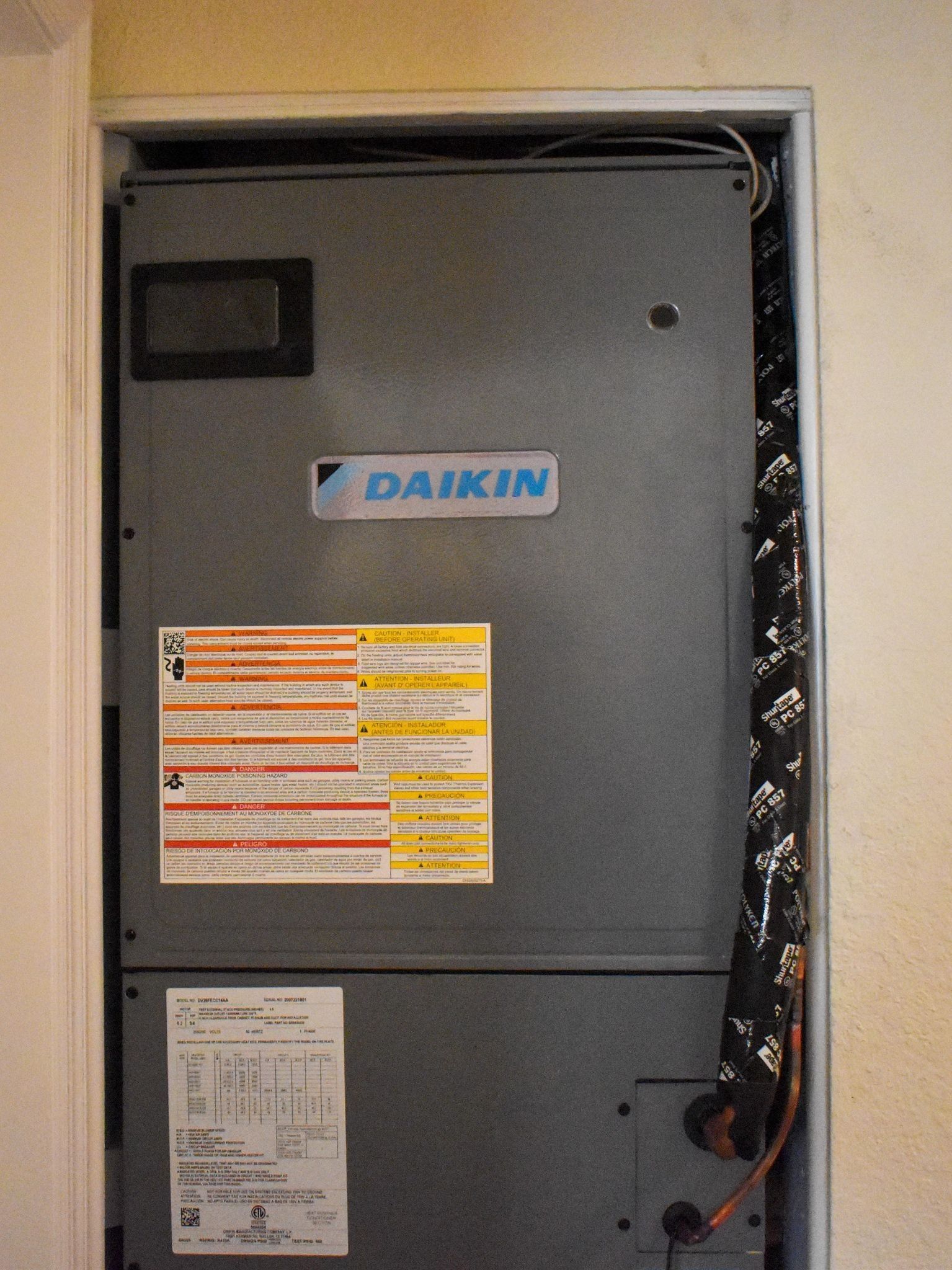 Gray Daikin HVAC air handler with warning labels, viewed inside a utility closet.