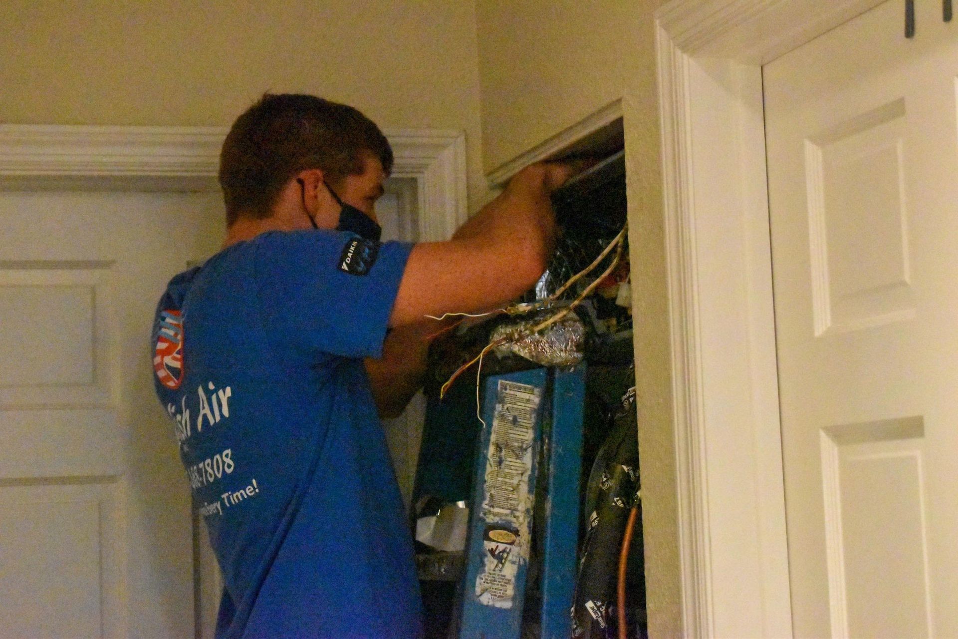 Person in blue shirt reaching into a closet full of hanging clothes.