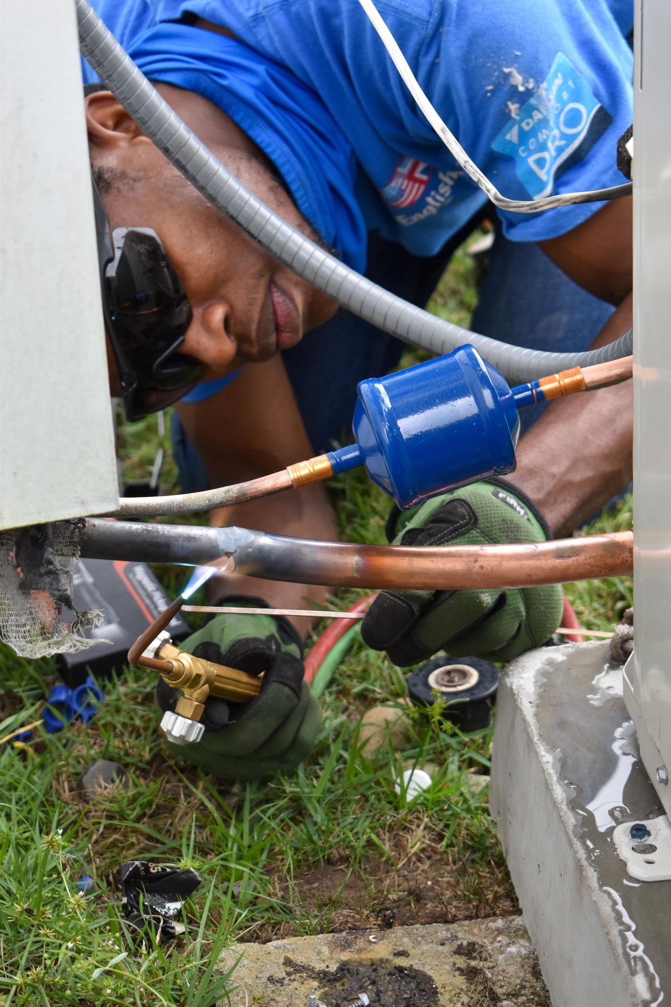 Worker using tools to repair a blue pipe in a grassy utility area