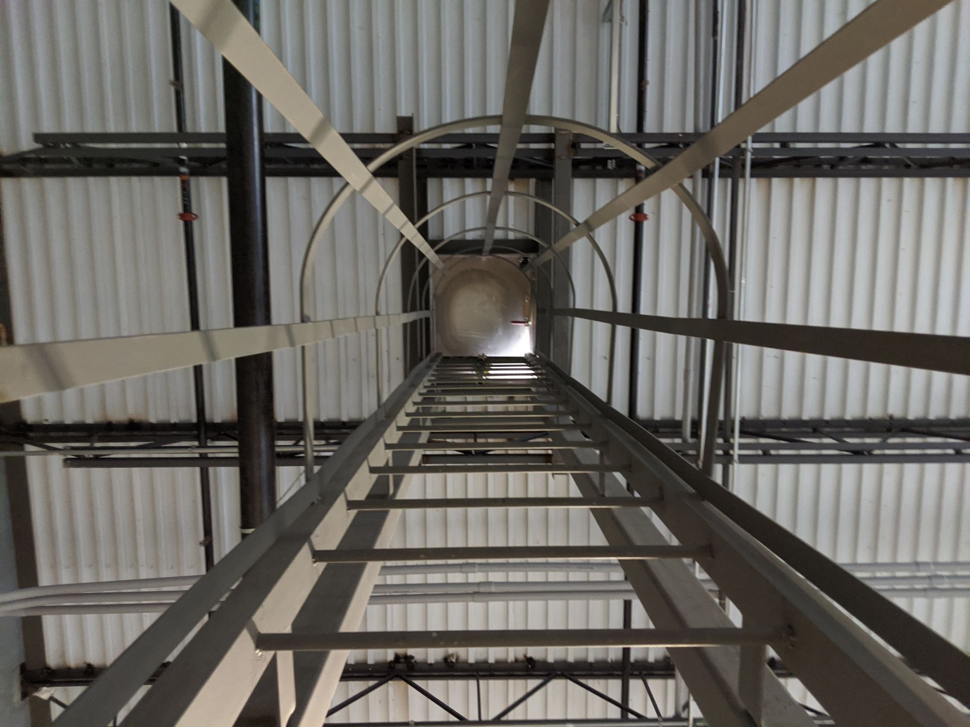 Looking up inside a tall metal ladder and cylindrical shaft in an industrial structure