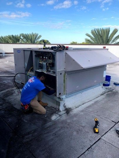 Technician kneeling beside an open rooftop HVAC unit on a flat roof, with tools nearby.