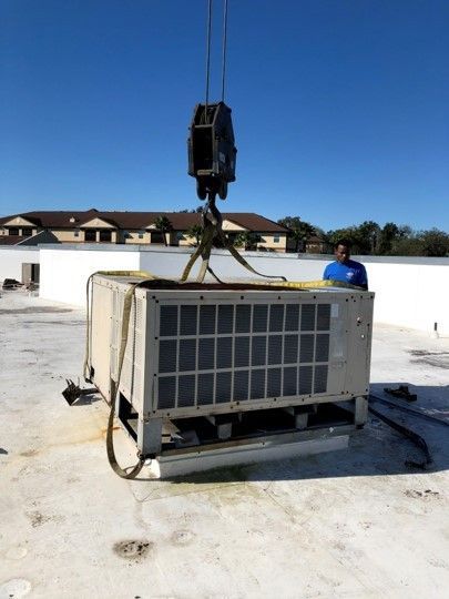 Industrial HVAC unit being lifted by crane onto a rooftop, with a worker standing nearby.