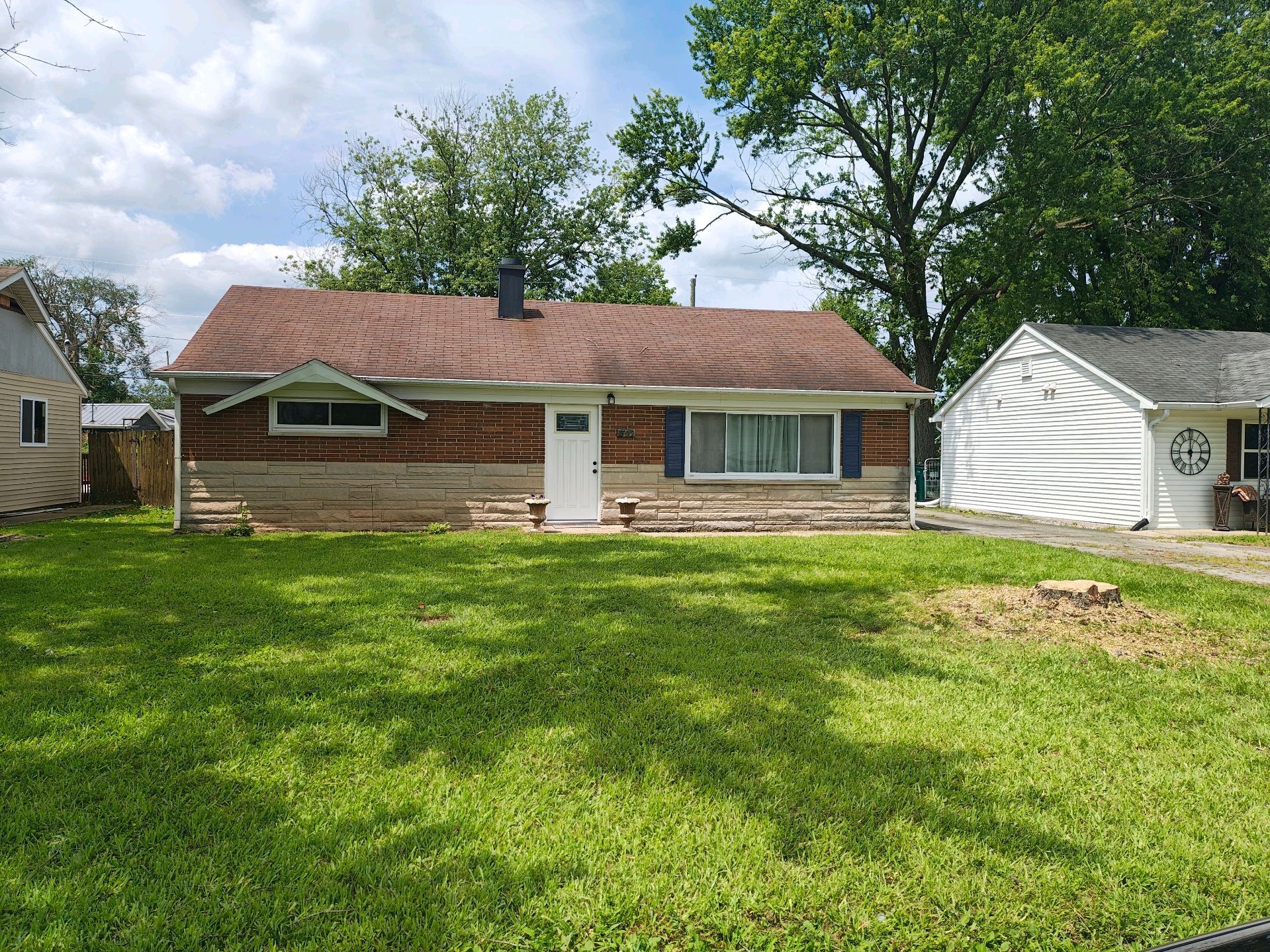Small, weathered house with a brown roof, white door, and green grass yard.