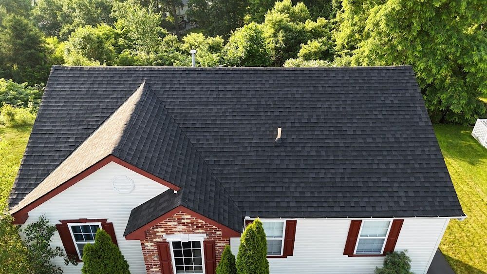 House with dark gray roof, white siding, and red shutters. Green trees in the background.