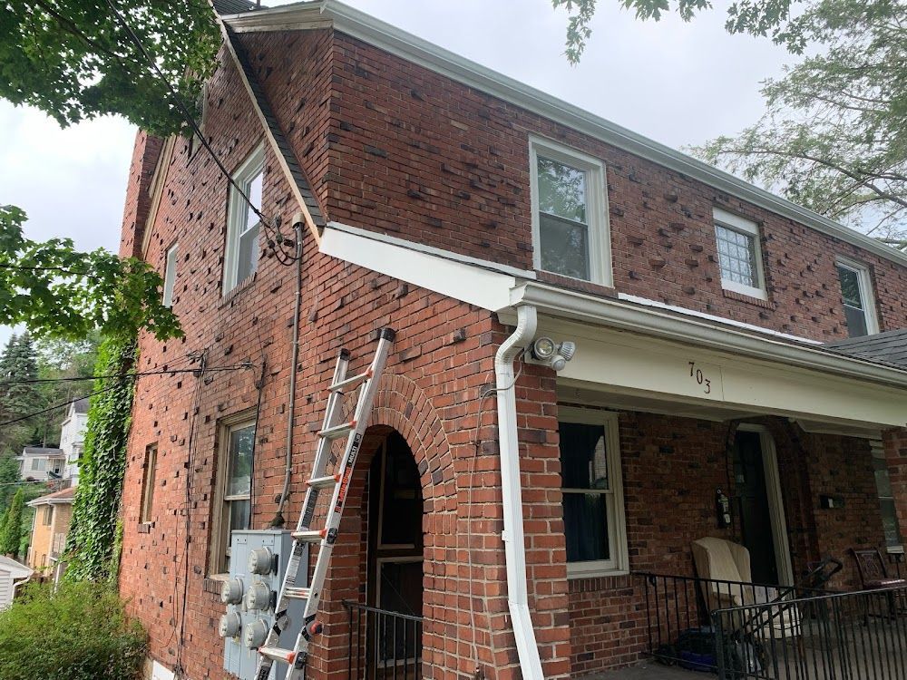 Red brick house with a ladder leaning against it. Gutters, windows, and an electrical box are visible.