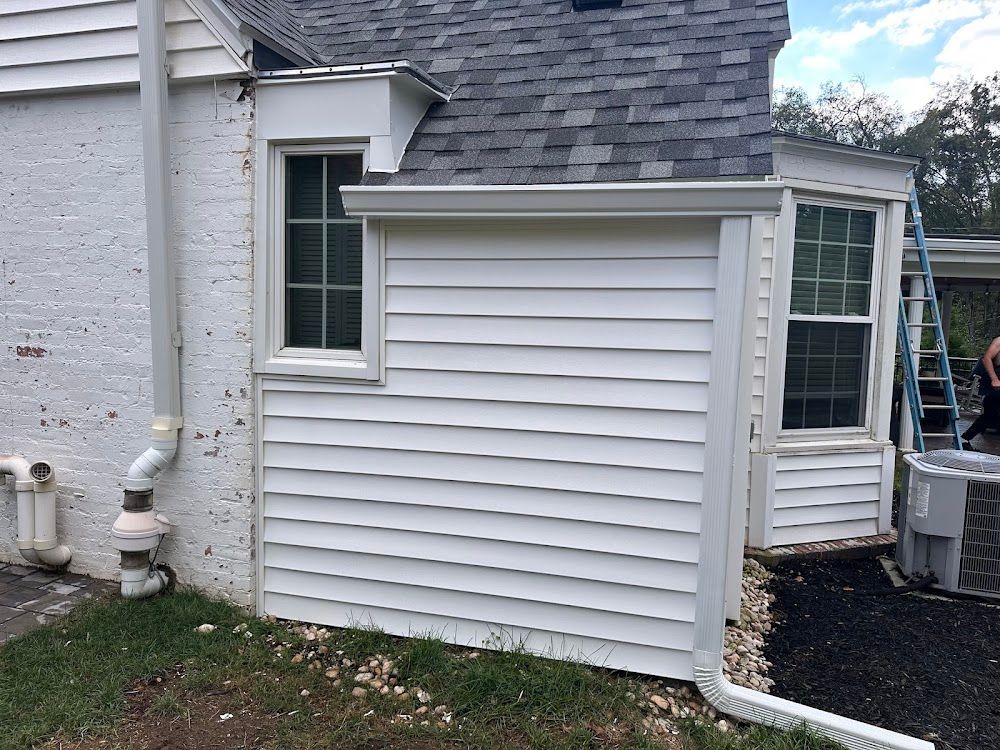 White house exterior with new siding, window, and gutters. A ladder leans against the right side.