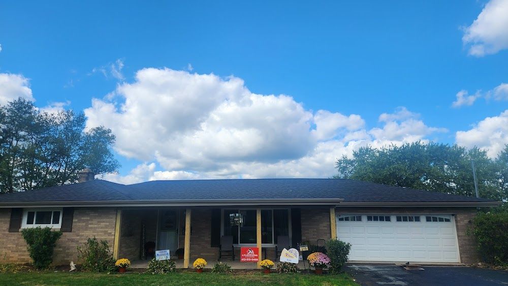 Single-story brick house with a dark roof and a white garage door against a cloudy blue sky.