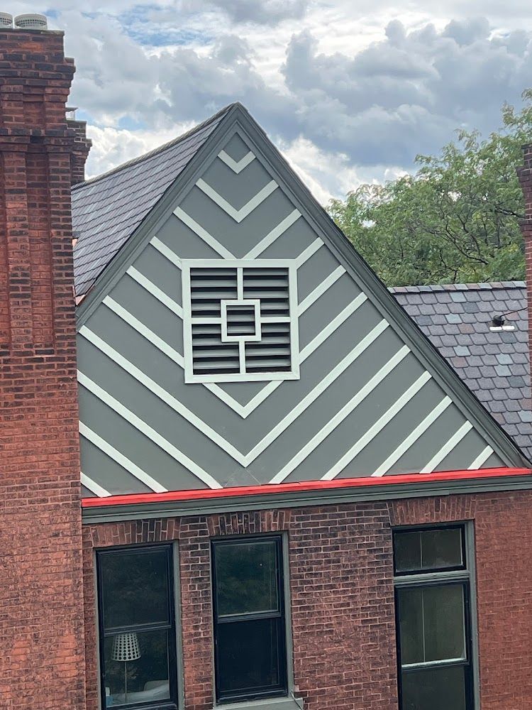 Brick building with grey and white gabled facade featuring a square vent and angled trim.