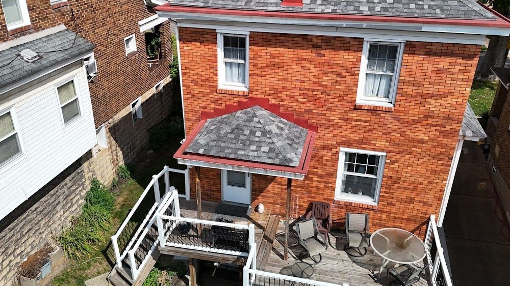 Brick house with porch and deck, nestled between other buildings on a hillside.