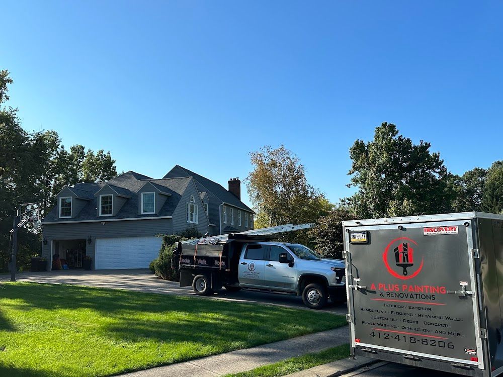 Gray house with a truck and trailer on the lawn; blue sky overhead.