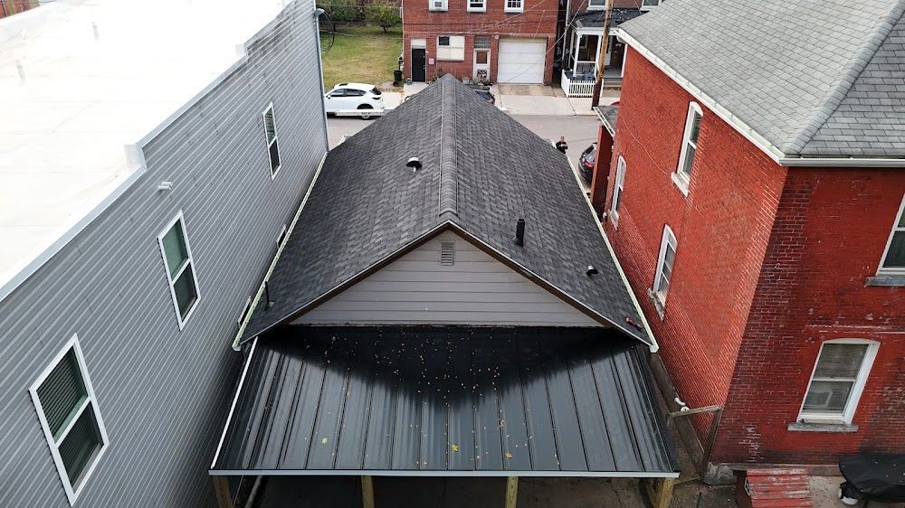 Aerial view of a narrow building with a dark roof nestled between a gray and a red building.