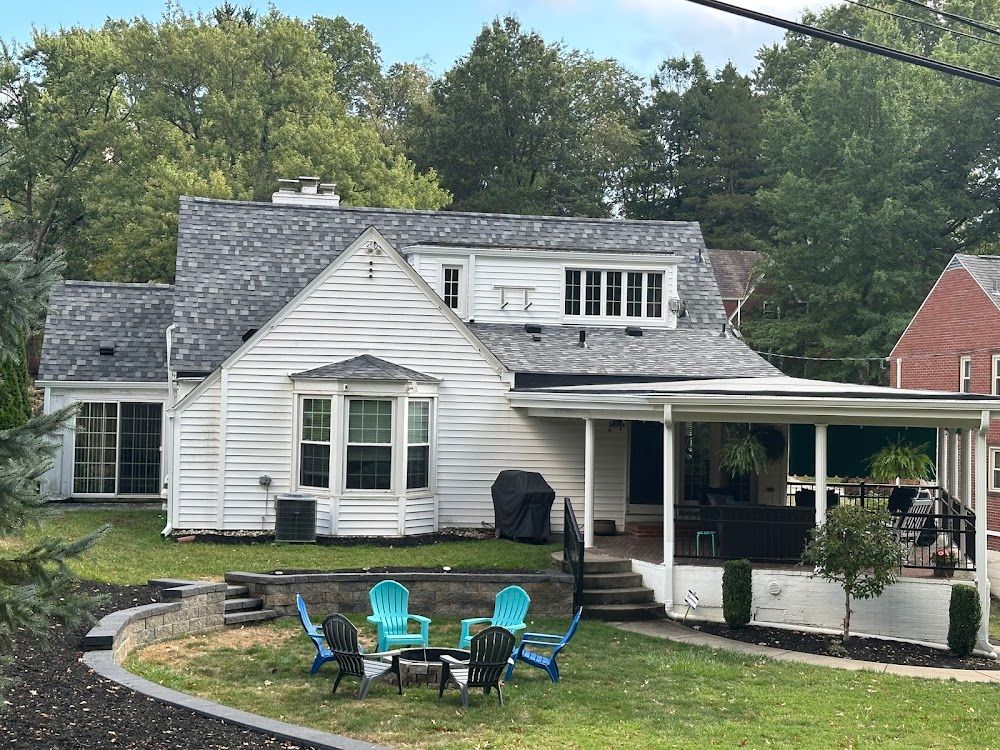 White house with gray roof, a porch, and lawn with blue chairs.