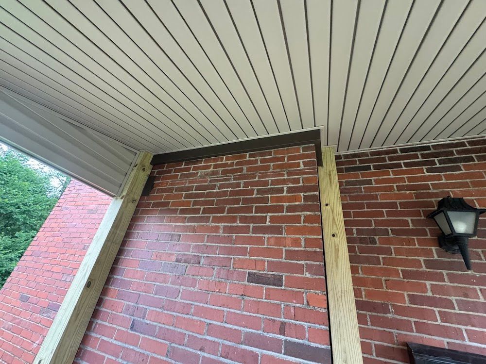 Brick wall with wooden beams supporting a covered porch ceiling. A light fixture is visible.