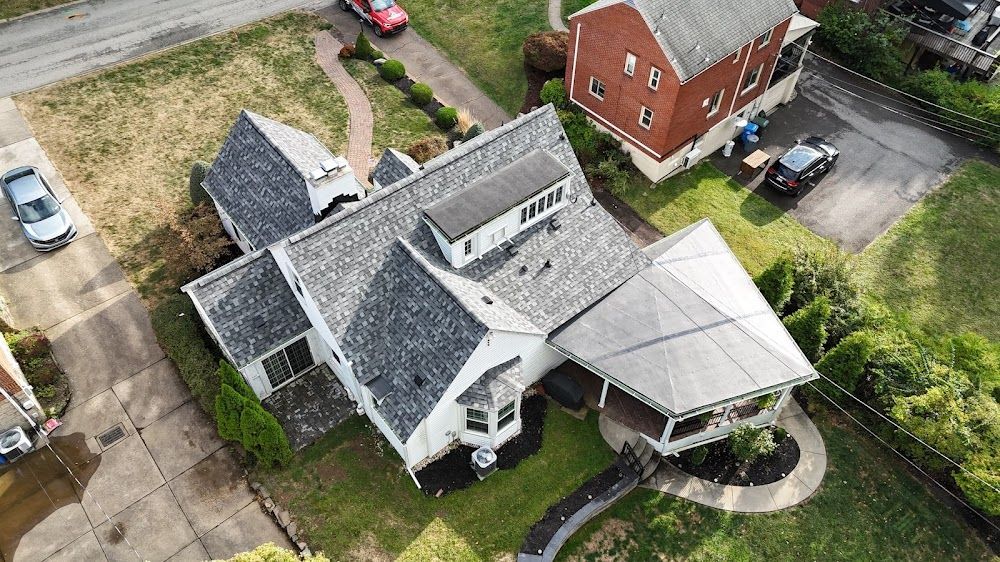 Aerial view of a white house with a gray roof and a porch. Cars and green lawn surround it.