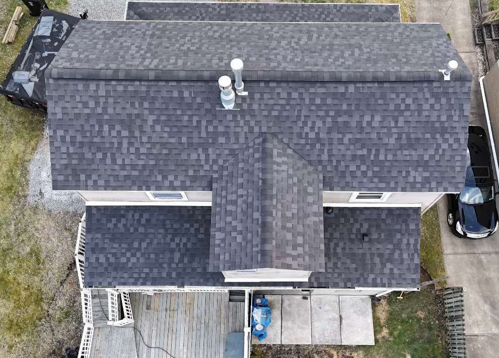 Overhead view of a house with a dark gray shingled roof, a car parked nearby, and a wooden deck.