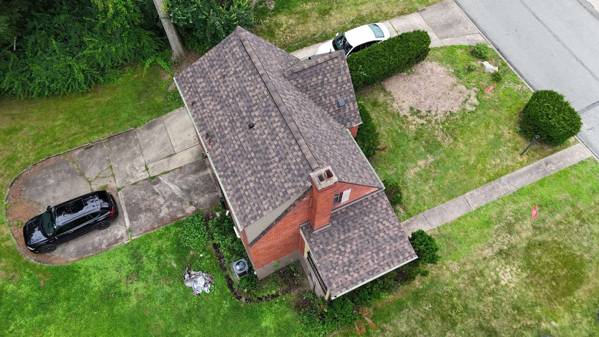 Overhead view of a house with a brown roof, red brick chimney, and two cars parked in the driveway.