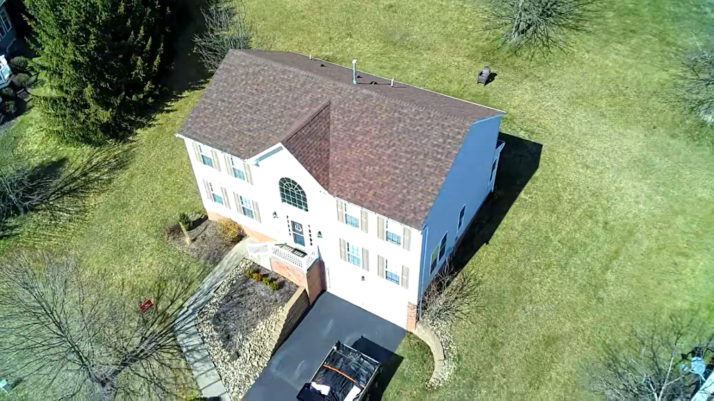 Aerial view of a two-story house with brown roof and white siding; black driveway.