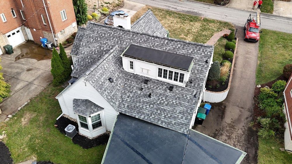 Overhead view of a house with a gray shingled roof, a dark roof section, and a white skylight.