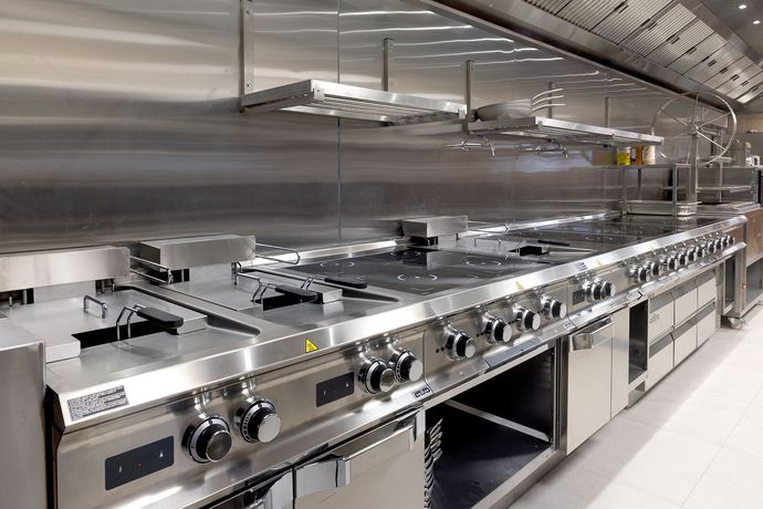 Cucina professionale con forni, piano cottura e cappe aspiranti in acciaio inox.
