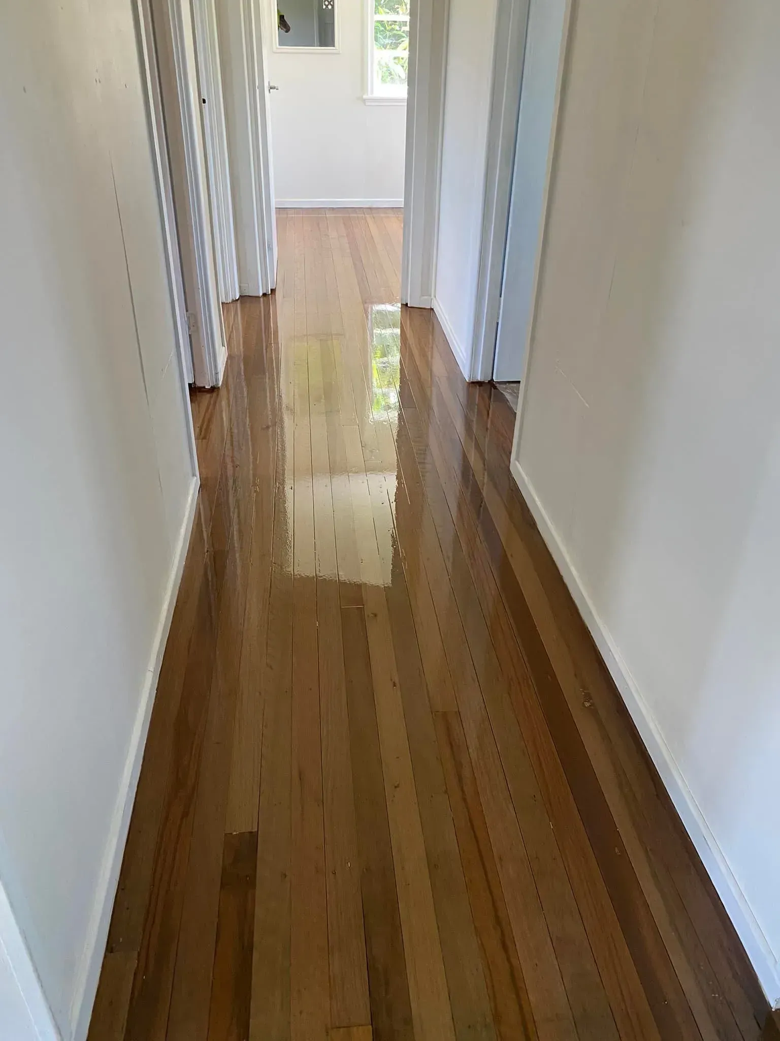 A Hallway With Hardwood Floors And White Walls Leading To A Bedroom — AJ's Cleaning & Floor Sanding In Woree, QLD