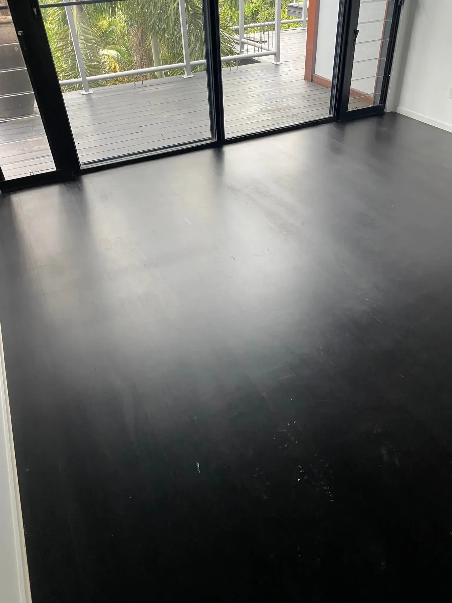A Room With A Black Floor And Sliding Glass Doors Leading To A Balcony — AJ's Cleaning & Floor Sanding In Woree, QLD