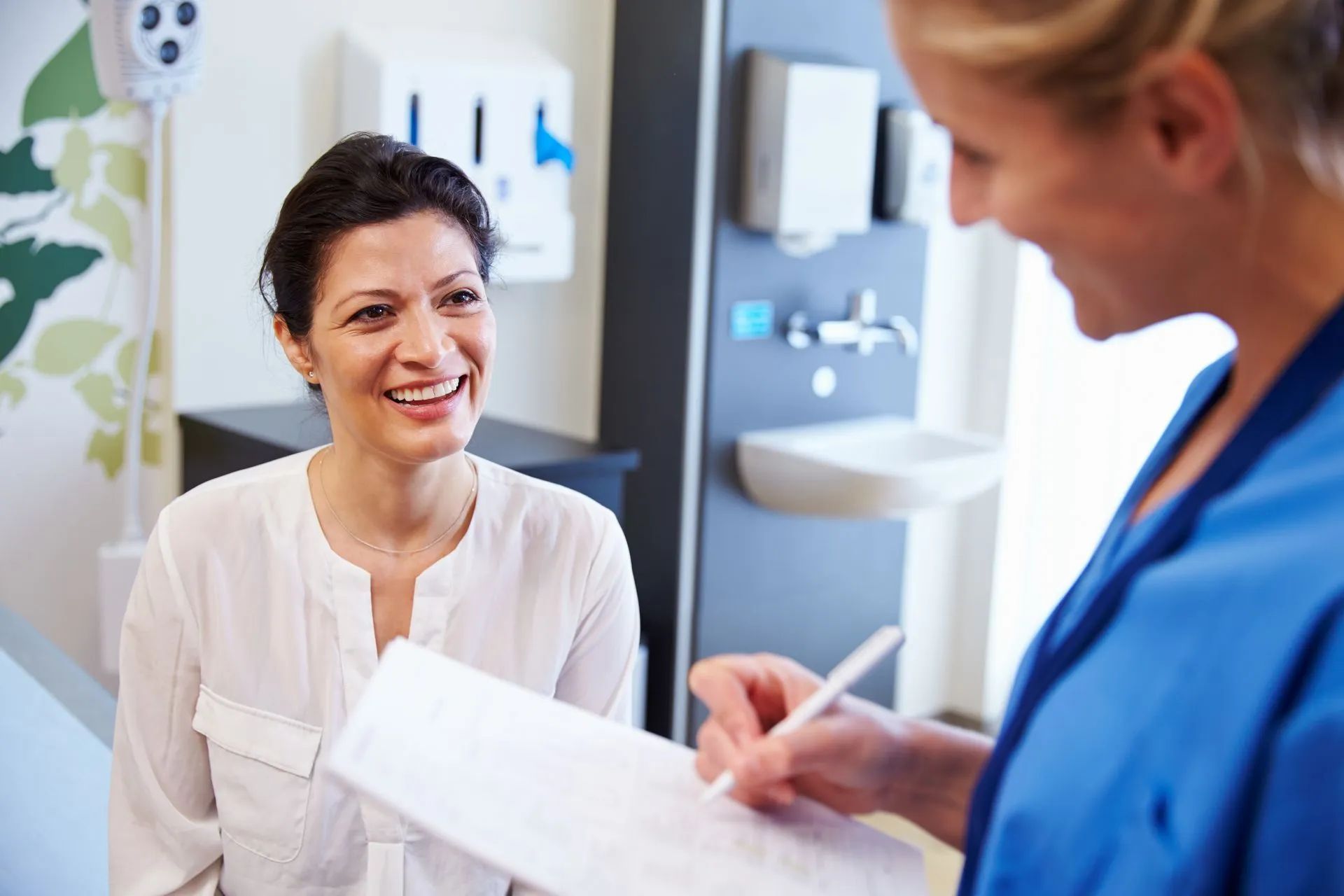 Doctor talking with patient in a clinic, holding a form and pen, both smiling.