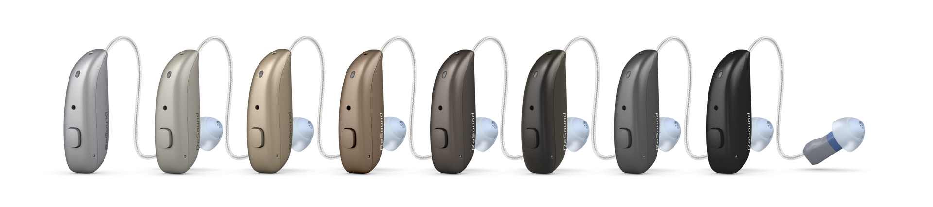 Several small hearing aids in white, beige, brown, gray, and black lined up on a white background.