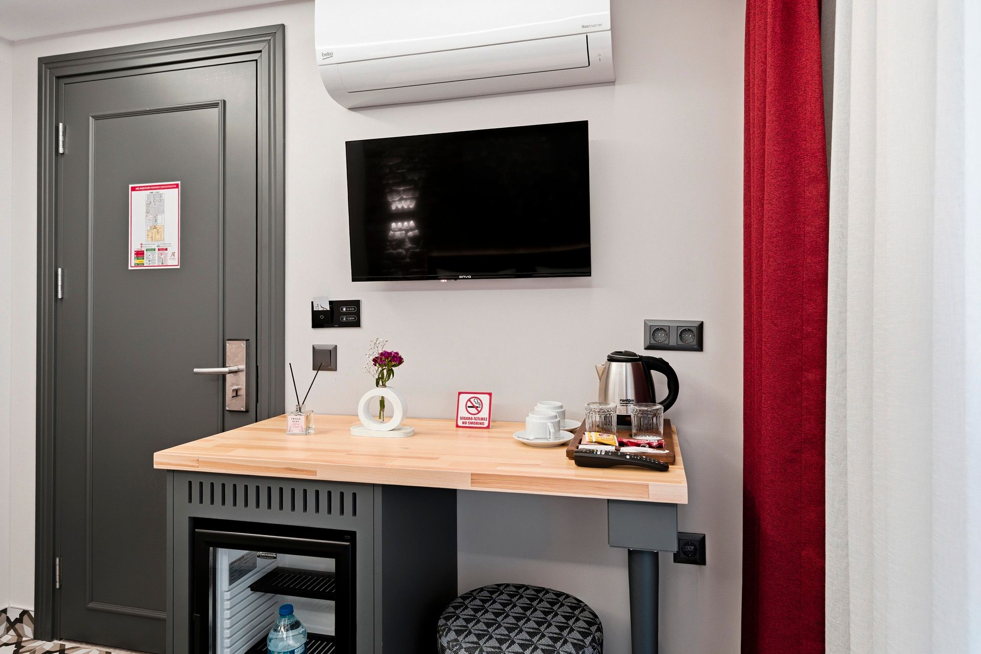 ARTELIST HOTEL | Hotel room desk with wall-mounted TV, air conditioner, and kettle on a wooden counter