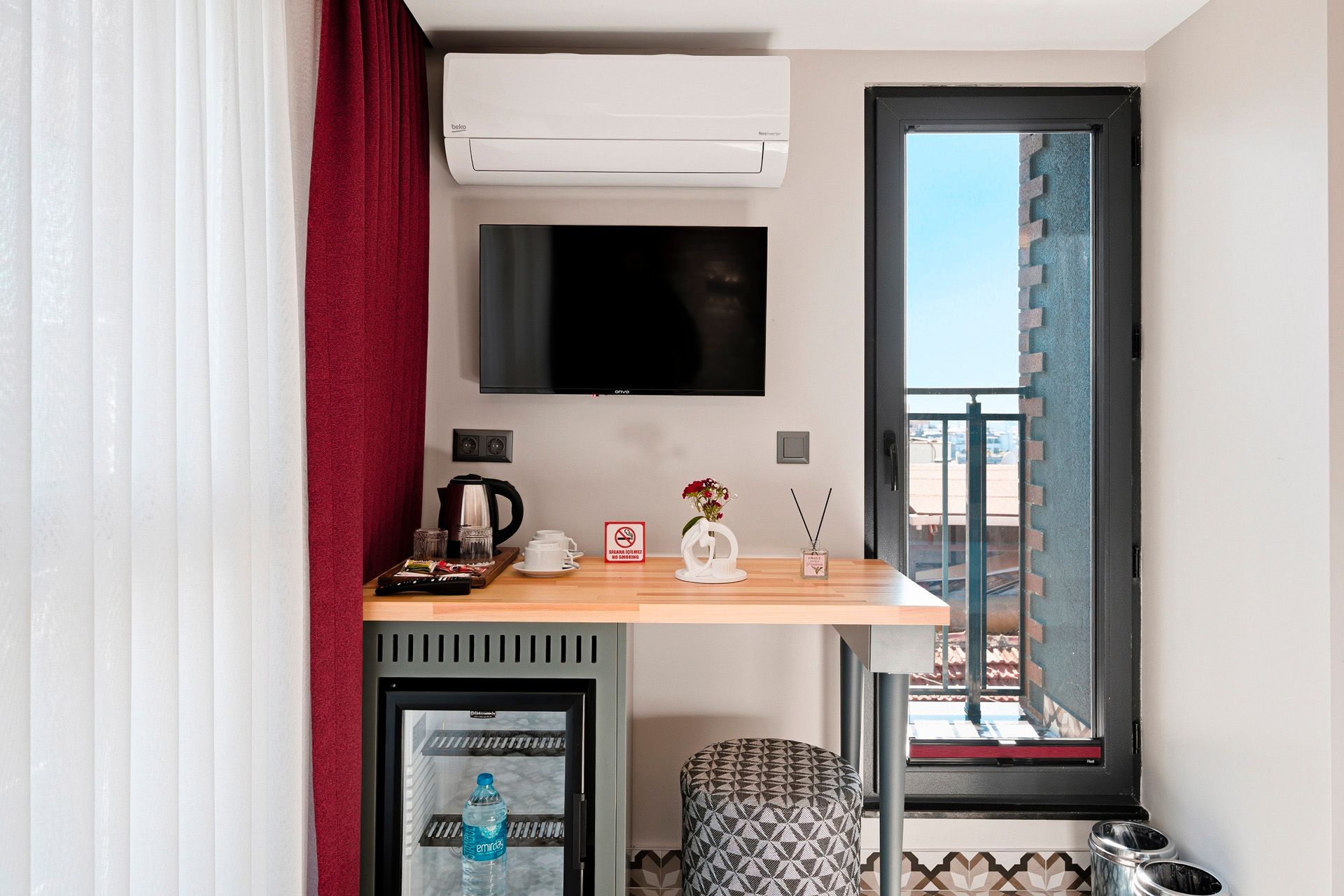 ARTELIST HOTEL | Compact hotel room desk with TV, coffee station, and balcony door overlooking a city view