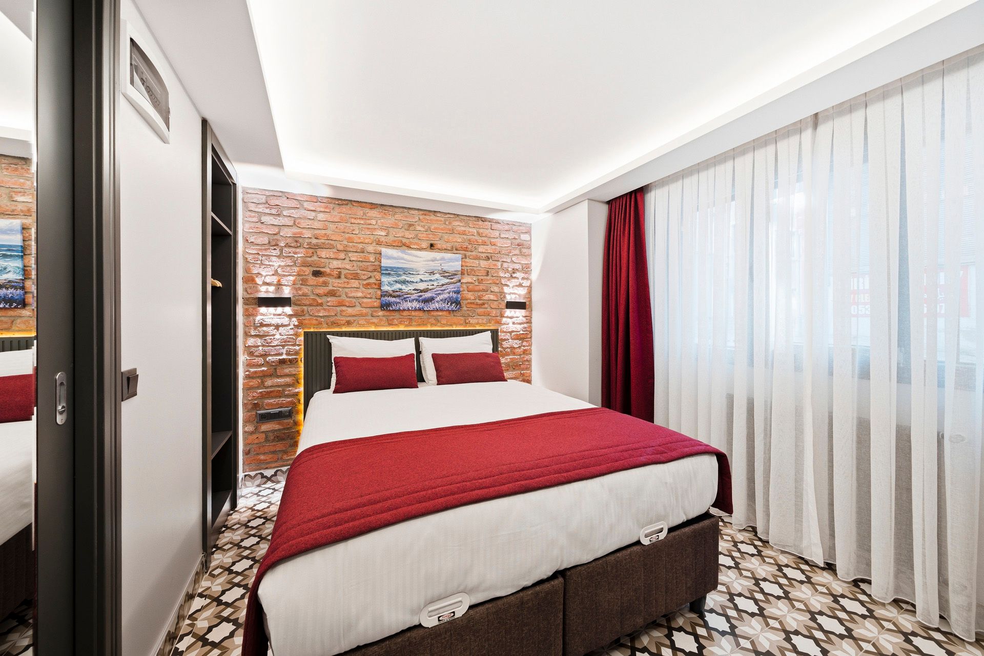 ARTELIST HOTEL | Modern hotel room with a double bed, red accents, patterned carpet, and sheer curtains