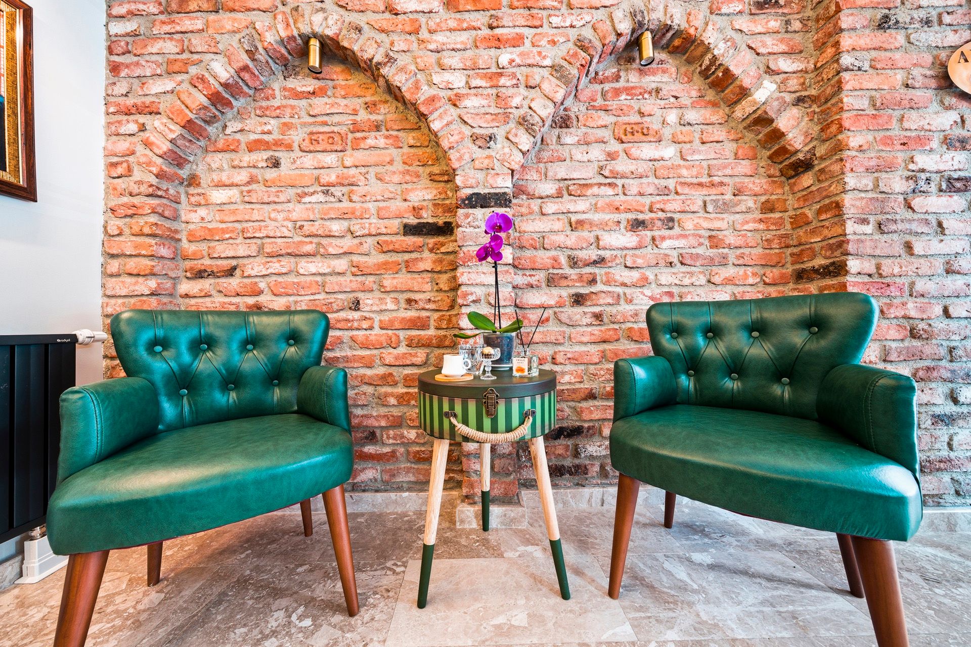ARTELIST HOTEL | Two teal armchairs by a brick wall, with a small table and purple flowers in the center.