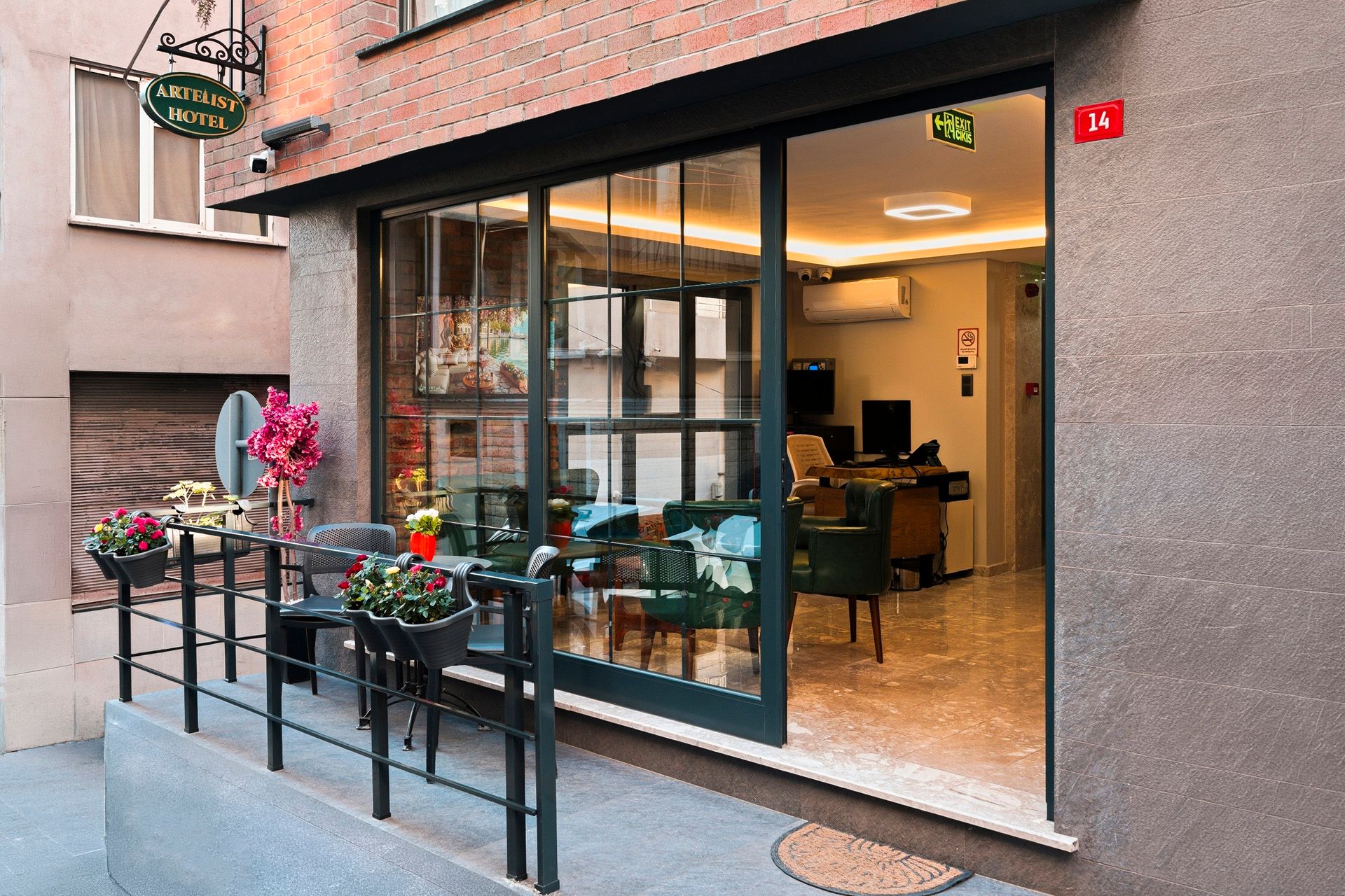 ARTELIST HOTEL | Small café storefront with glass door, outdoor flowers, and a lit interior view