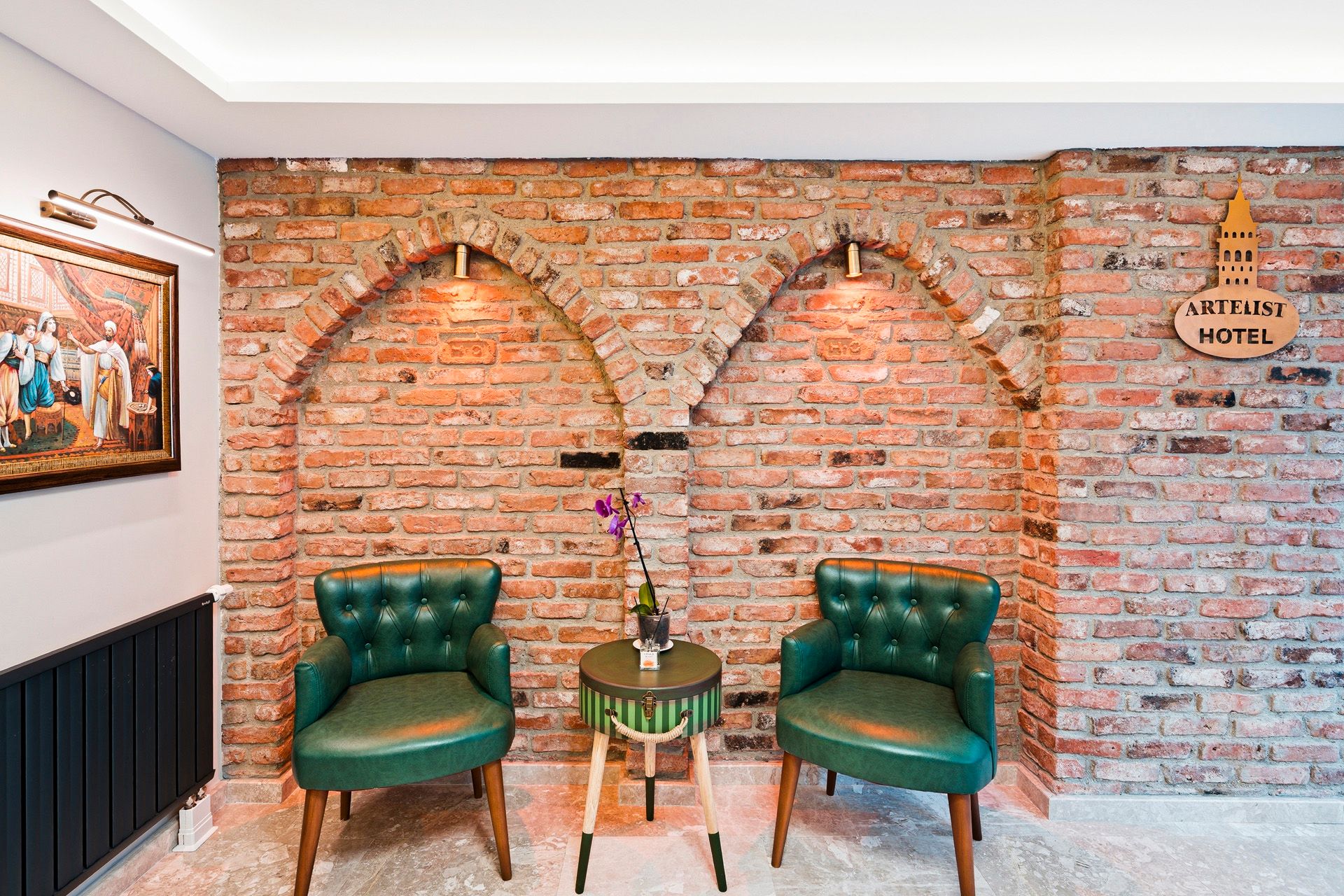 ARTELIST HOTEL | Cozy seating area with two green chairs, round table, and exposed brick wall with arched accents