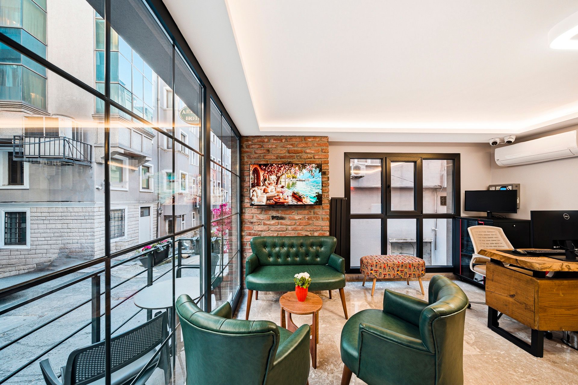 ARTELIST HOTEL | Bright modern lounge with green chairs, a sofa, large windows, and a piano by a TV display