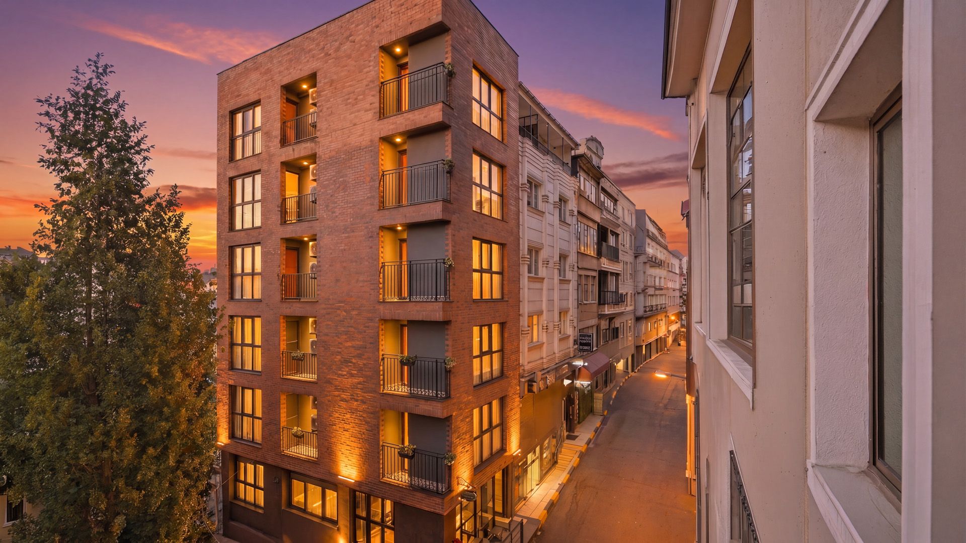 ARTELIST HOTEL | Modern apartment buildings on a city street at sunset, with warm window lights and a pink sky