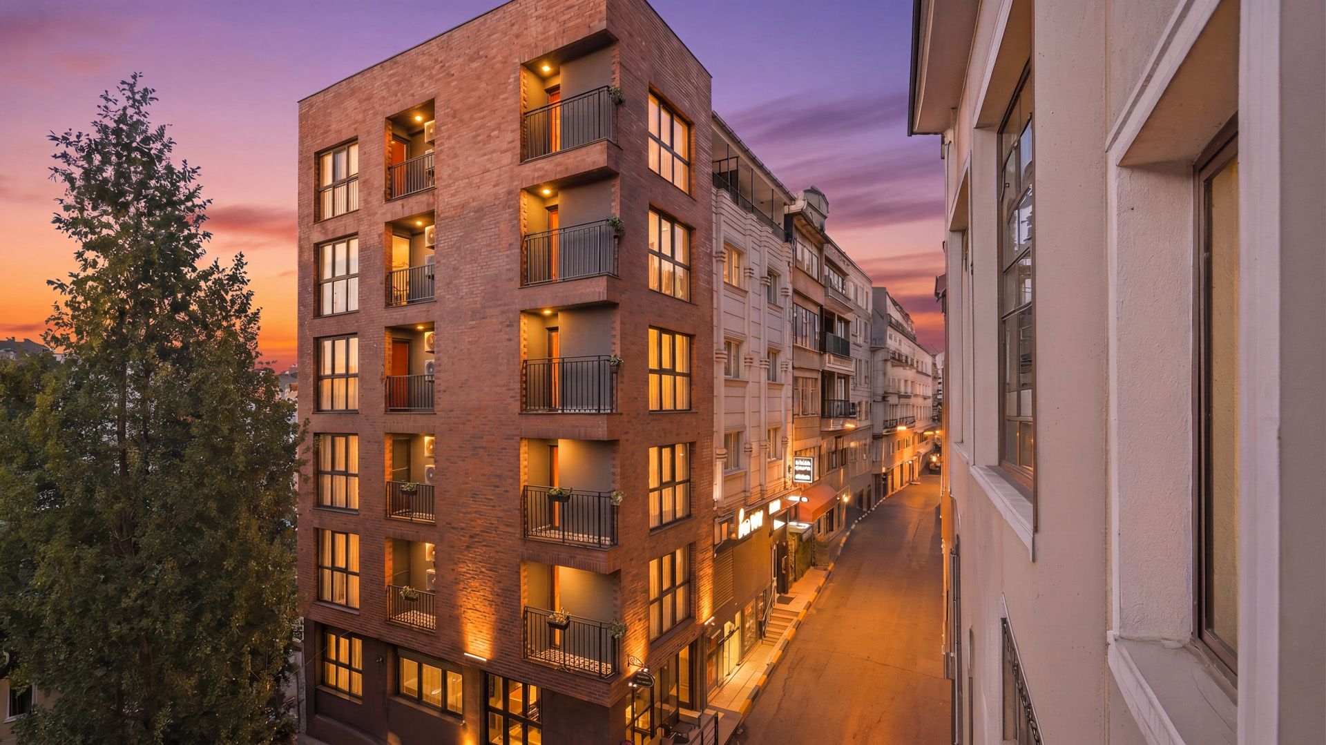 ARTELIST HOTEL | Modern apartment buildings at sunset on a narrow city street, with warm lights glowing from windows.