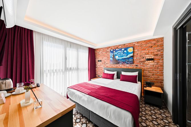 ARTELIST HOTEL | Modern bedroom with red brick accent wall, bed, wooden desk, and floor-to-ceiling window